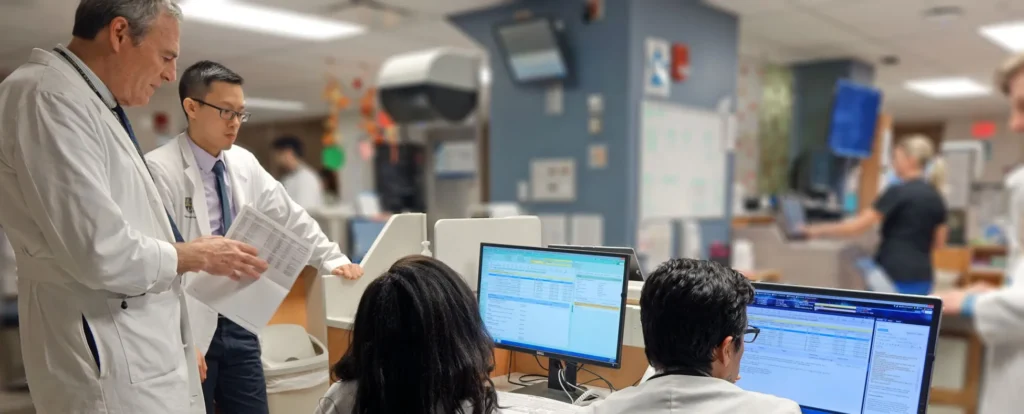 Healthcare professionals discussing patient records at a workstation with medical coding software on computer screens – certified medical coding in action.